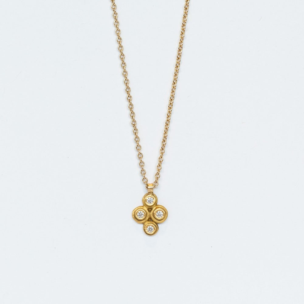 A yellow gold cable chain suspending a petite gold pendant made up of four bezel-set white diamonds in a floral motif.