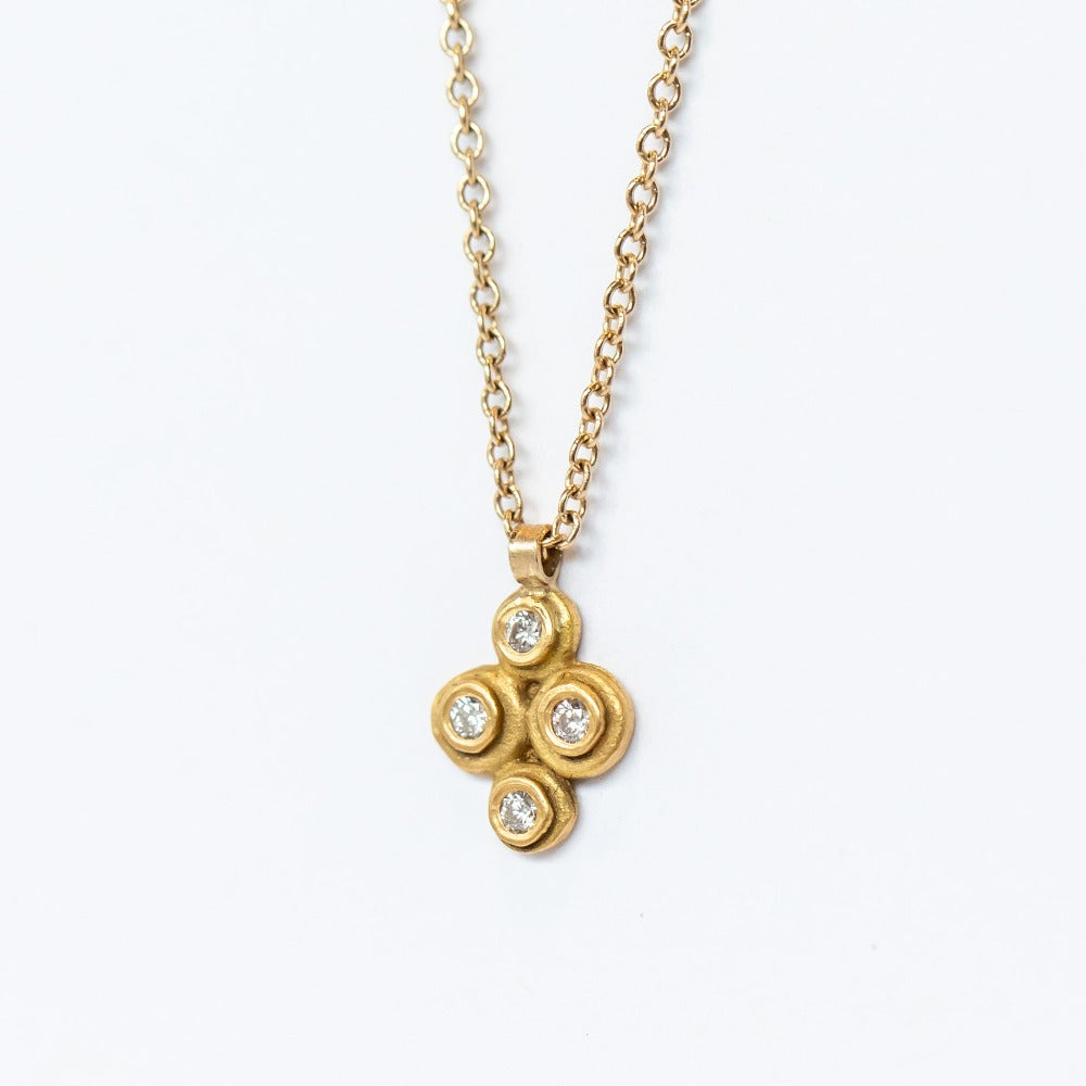 A yellow gold cable chain suspending a petite gold pendant made up of four bezel-set white diamonds in a floral motif.