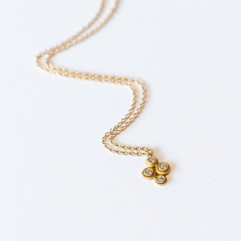 A yellow gold cable chain suspending a petite gold pendant made up of four bezel-set white diamonds in a floral motif.