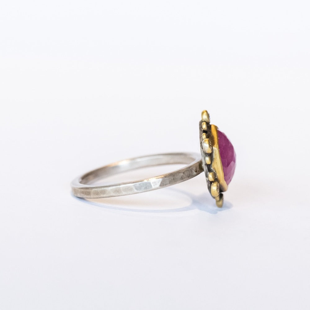 A rose cut, hexagonal shaped pink star sapphire is bezel set in yellow gold, surrounded by a halo of white diamond and yellow gold dot accents on a blackened silver ring. Side view.