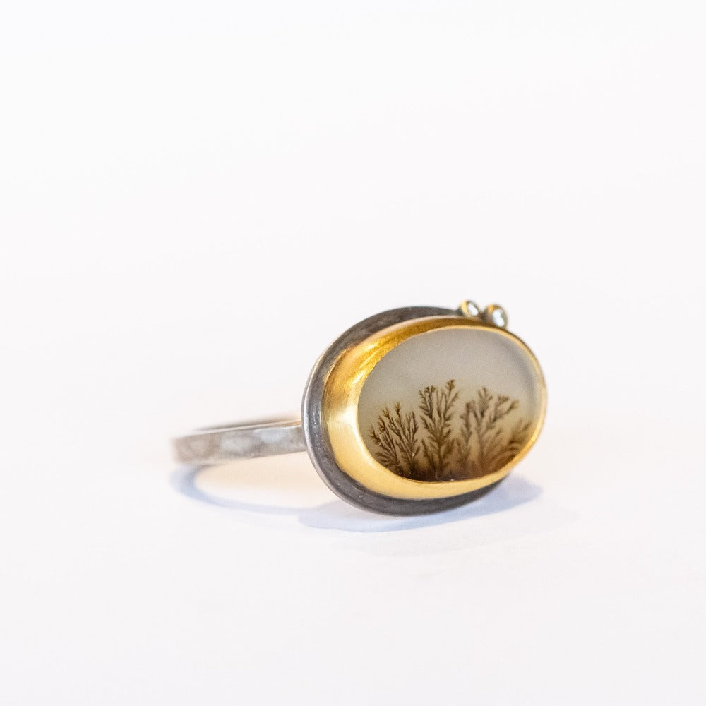 A horizontal oval dendritic agate ring with two diamond accents. Set in yellow gold bezel on a sterling silver ring. Angle view.