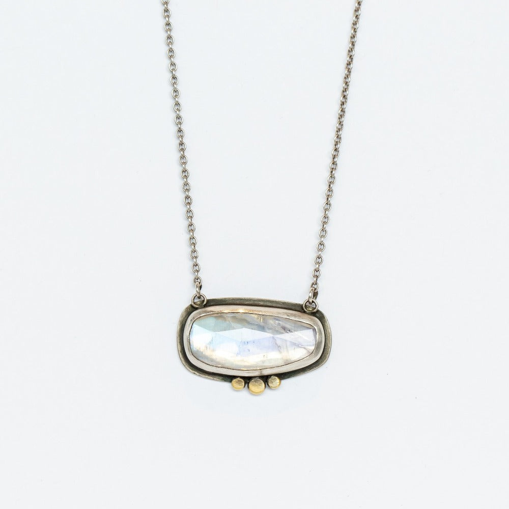 A horizontal rose cut moonstone is set in a sterling silver bezel with dainty gold dot accents along the bottom edge. It's stationed in a sterling silver cable chain necklace.