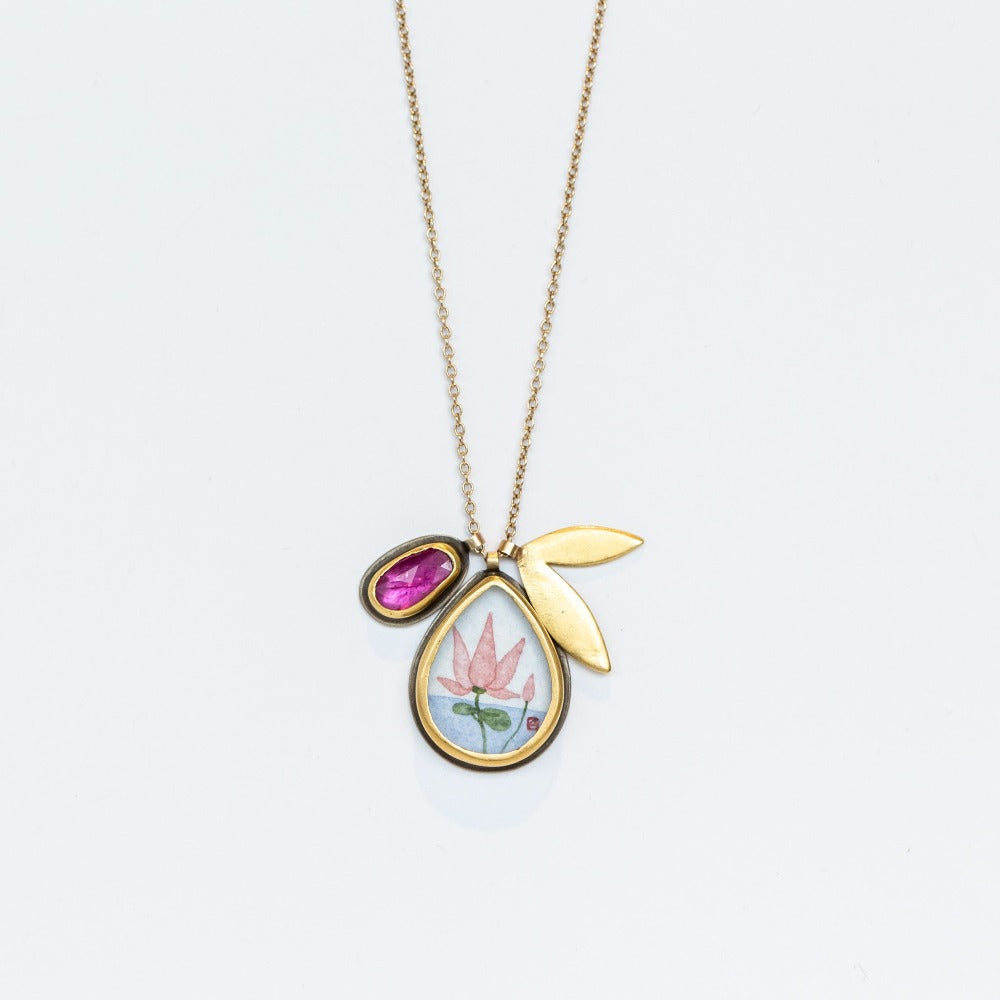 A hand painted, teardrop shape charm with a lotus is suspended from a simple cable chain with a bezel set ruby charm and petal-shaped charm.