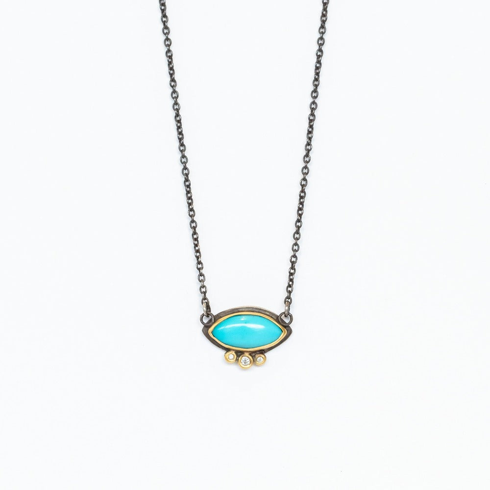 A marquise-cut bright blue turquoise gemstone pendant. The gem is set in a yellow gold bezel, with three gold bezel set diamonds underneath it, all backed in sterling silver on an oxidized sterling silver chain.
