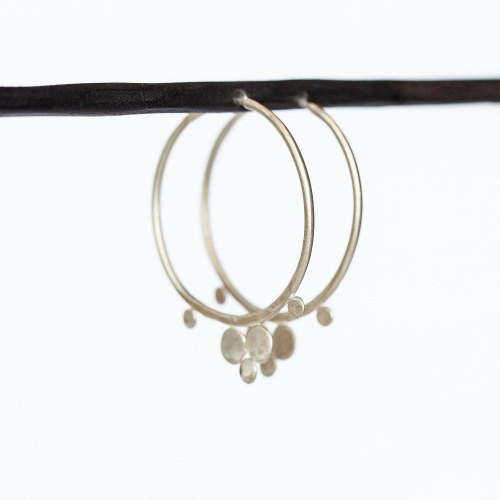 A pair of brushed, hammered silver hoop earrings with flat silver dot trio accents.