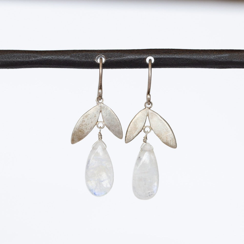 A pair of drop earrings crafted of sterling silver, featuring a petal shaped top with a polished, teardrop moonstone dangle underneath.