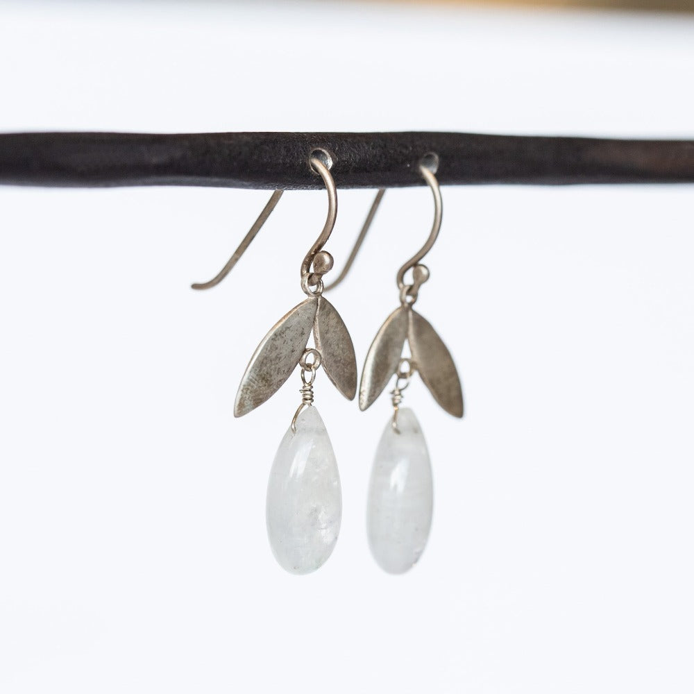 A pair of drop earrings crafted of sterling silver, featuring a petal shaped top with a polished, teardrop moonstone dangle underneath.
