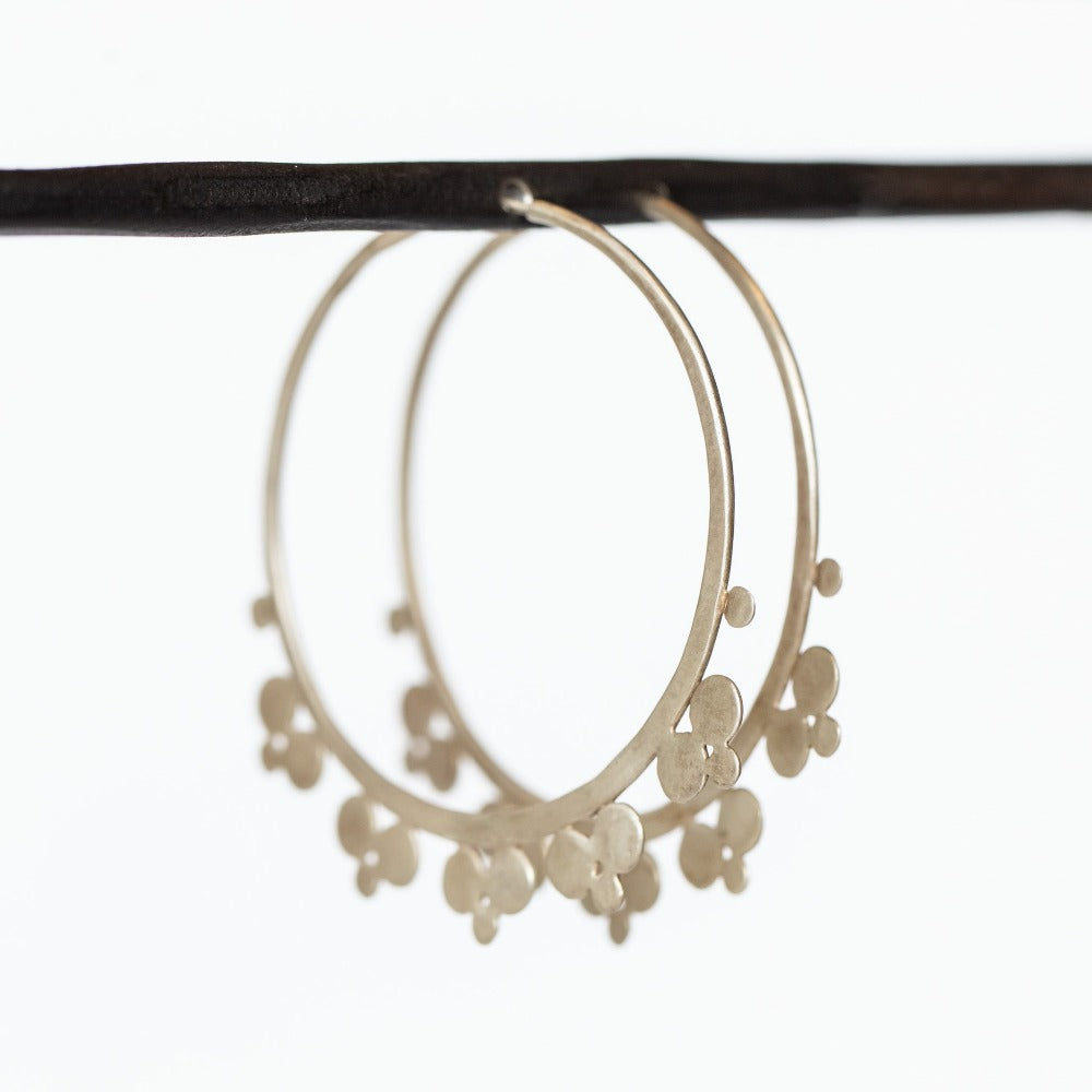 A pair of large hammered silver hoop earrings featuring spaced out trios of flat silver dots along the outside edge.