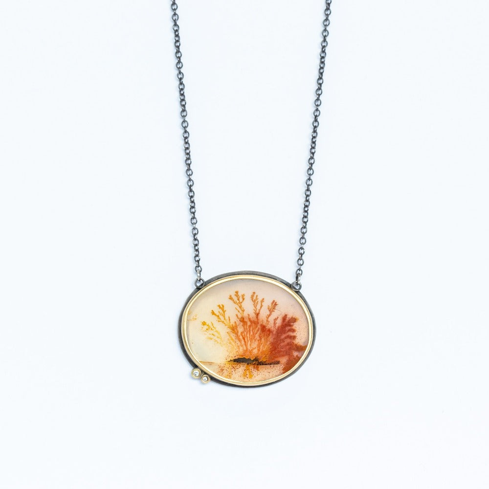 An oval shaped, orange dendritic agate is bezel set in yellow gold with two diamond accents. Necklace is sterling silver.