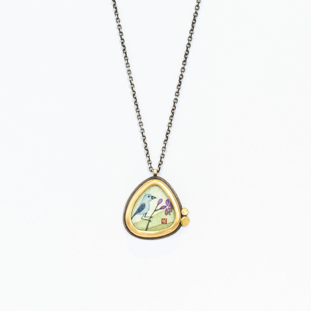 Ananda Khalsa pendant necklace featuring a hand painted bluebird on a branch, bezel set in yellow gold with tiny dot accents on a sterling silver chain.