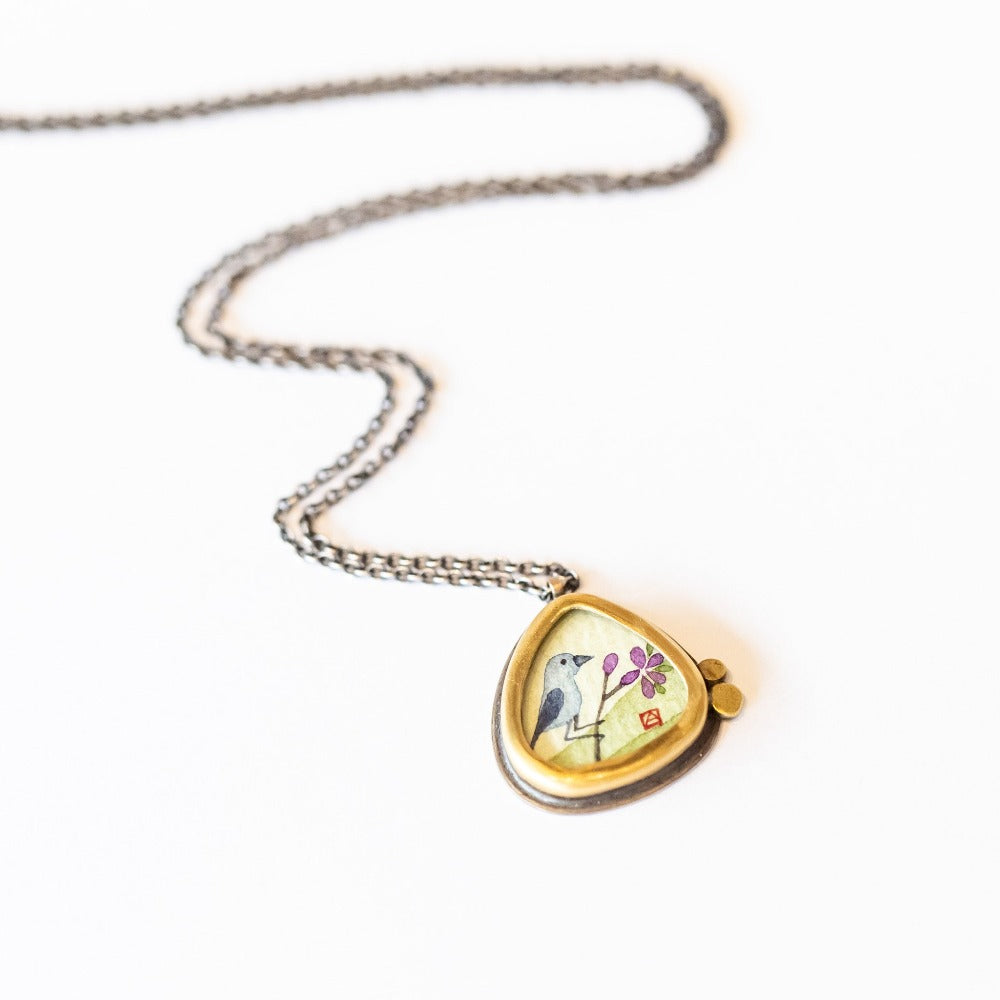 Ananda Khalsa pendant necklace featuring a hand painted bluebird on a branch, bezel set in yellow gold with tiny dot accents on a sterling silver chain.