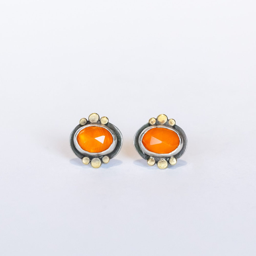 Dainty, faceted orange oval carnelian stud earrings with gold dot accents on the bezel. Set in sterling silver with post backs.