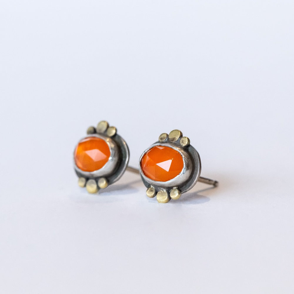 Dainty, faceted orange oval carnelian stud earrings with gold dot accents on the bezel. Set in sterling silver with post backs.