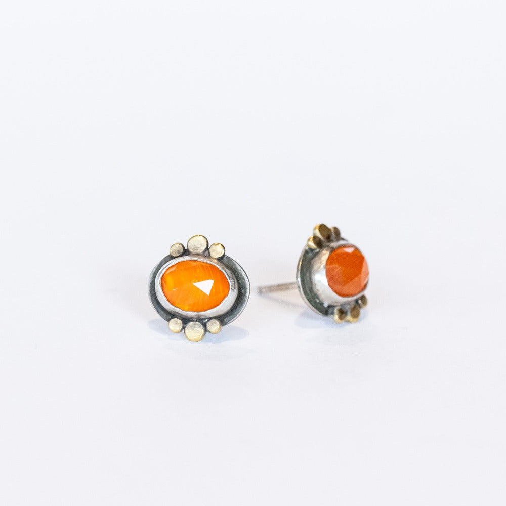 Dainty, faceted orange oval carnelian stud earrings with gold dot accents on the bezel. Set in sterling silver with post backs.
