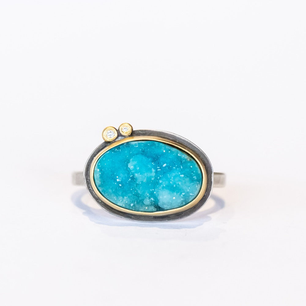 A bright, turquoise blue surface cut chrysocolla drusy ring set in a yellow gold bezel with two tiny diamond accents, on a sterling silver ring.