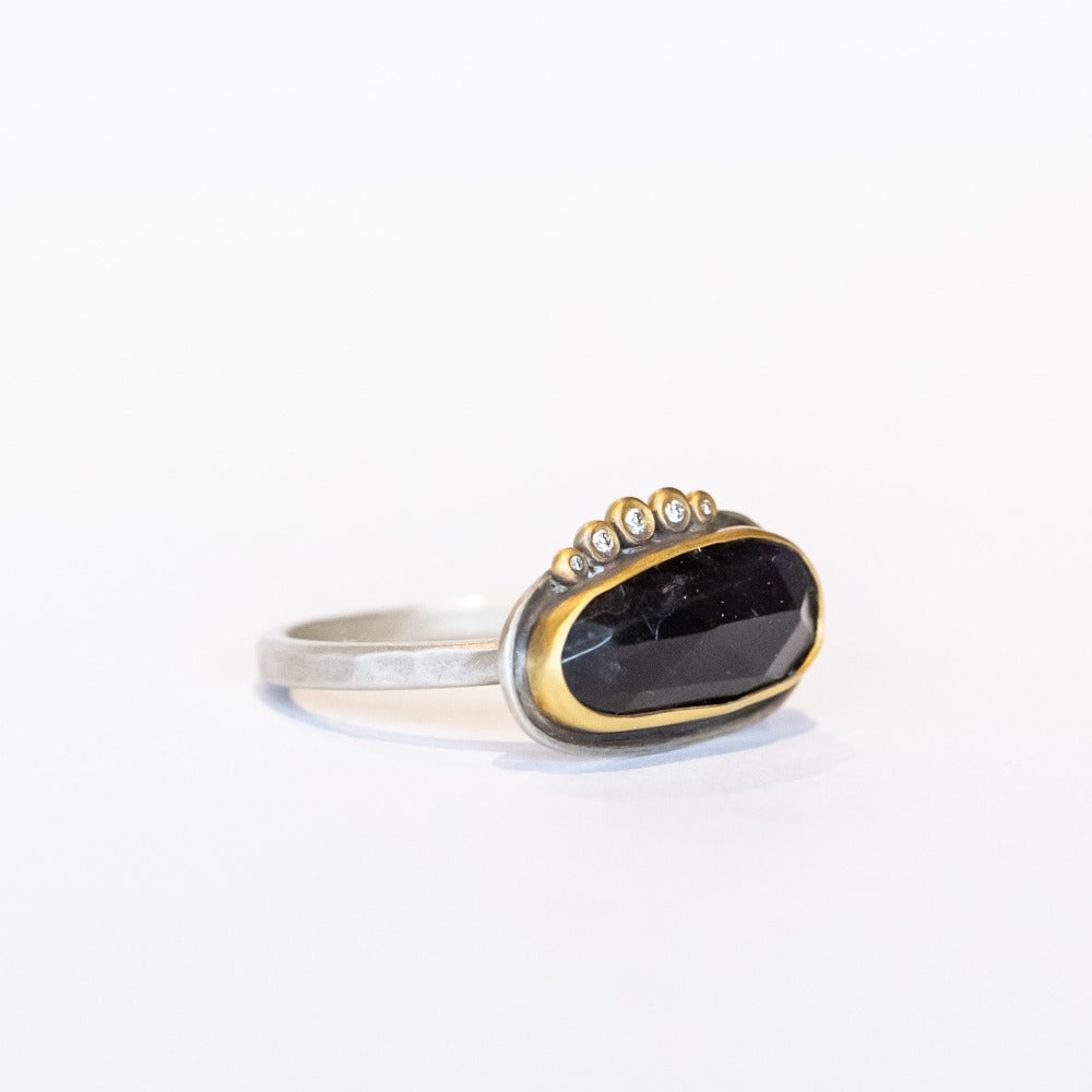 An elongated, rose cut labradorite gemstone in deep blue is set horizontally on this sterling silver ring. The gem is surrounded in a yellow gold bezel and accented along one edge with five petite diamonds.