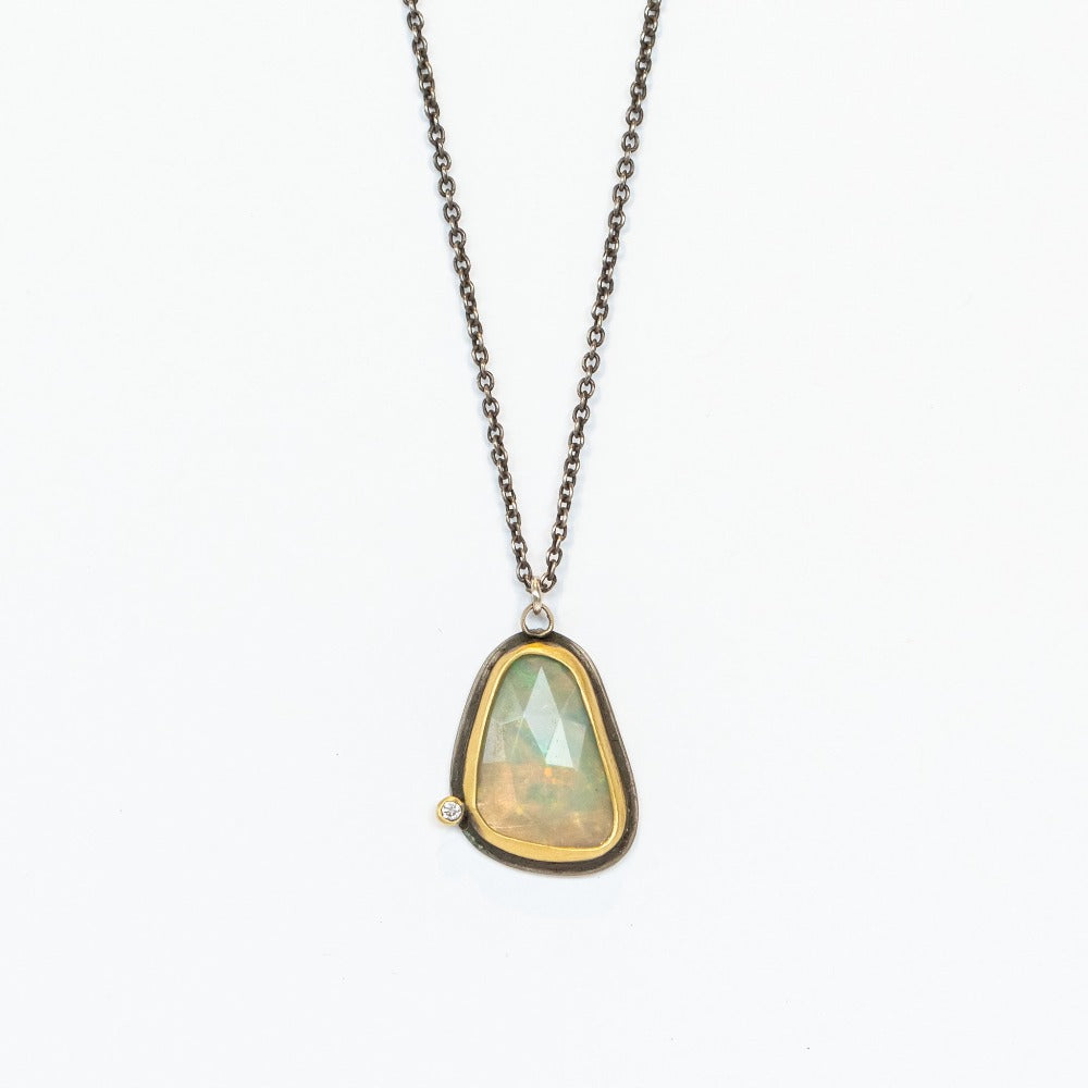 An asymmetrical teardrop shaped opal pendant, bezel set in yellow gold backed by oxidized silver, with one tiny diamond accent on an oxidized silver necklace chain.