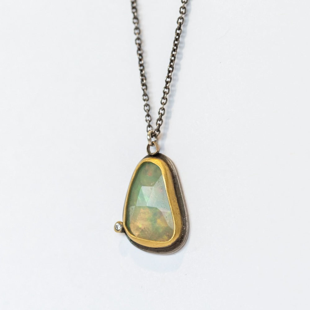 An asymmetrical teardrop shaped opal pendant, bezel set in yellow gold backed by oxidized silver, with one tiny diamond accent on an oxidized silver necklace chain.