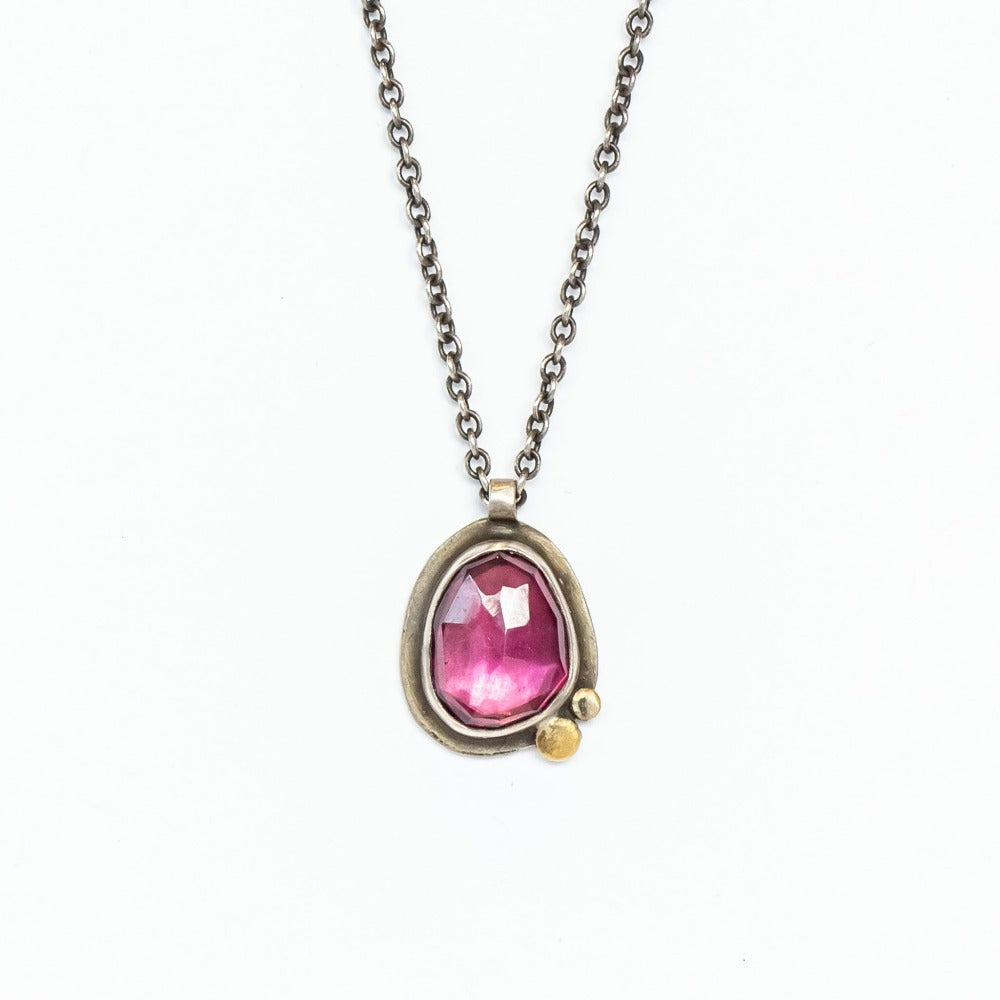 An asymmetrical teardrop shaped garnet is set in oxidized sterling silver with small gold dot accents.