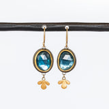 Oval rose cut London Blue Topaz gemstones are bezel set in yellow gold with sterling silver backs, with petite leaf-shaped gold dangles in these Ananda Khalsa drop earrings.