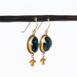 Oval rose cut London Blue Topaz gemstones are bezel set in yellow gold with sterling silver backs, with petite leaf-shaped gold dangles in these Ananda Khalsa drop earrings.