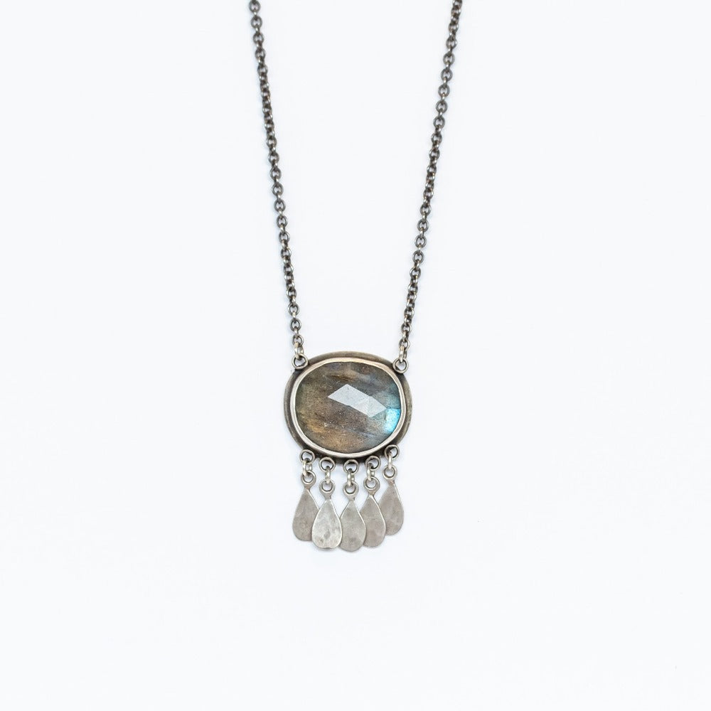 A large oval labradorite gemstone is bezel set in sterling silver with five hammered silver teardrop charms on this Ananda Khalsa necklace.