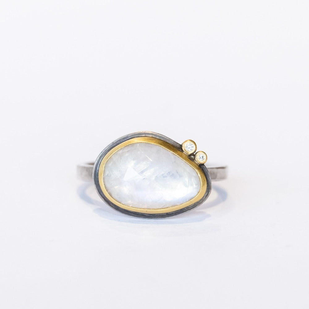 An asymmetrical, milky white rainbow moonstone tops this sterling silver ring from Ananda Khalsa. The gem is set in yellow gold and accented by two tiny, bezel set diamonds.