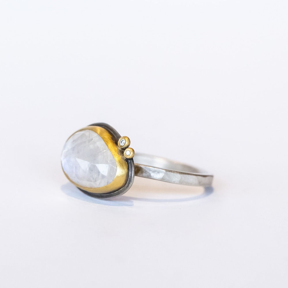 An asymmetrical, milky white rainbow moonstone tops this sterling silver ring from Ananda Khalsa. The gem is set in yellow gold and accented by two tiny, bezel set diamonds.