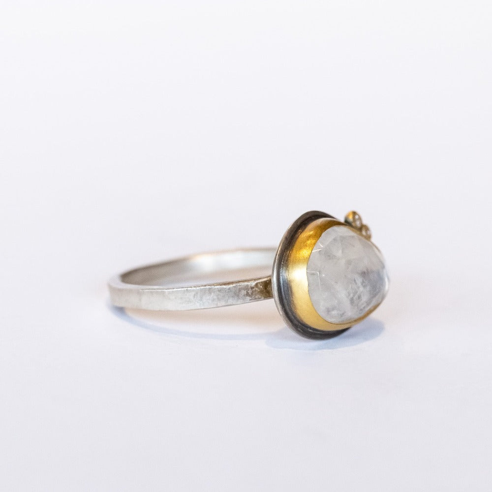 An asymmetrical, milky white rainbow moonstone tops this sterling silver ring from Ananda Khalsa. The gem is set in yellow gold and accented by two tiny, bezel set diamonds.