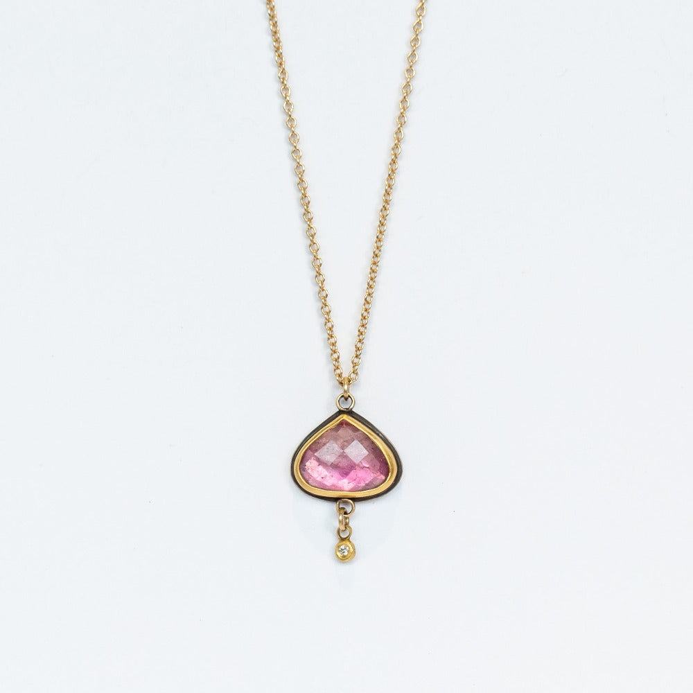 A yellow gold chain necklace with a wide teardrop, rose cut pink tourmaline in a 22k yellow gold bezel backed by oxidized sterling silver. A tiny bezel-set diamond charm dangles freely from the base.