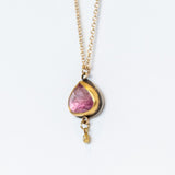 A yellow gold chain necklace with a wide teardrop, rose cut pink tourmaline in a 22k yellow gold bezel backed by oxidized sterling silver. A tiny bezel-set diamond charm dangles freely from the base.