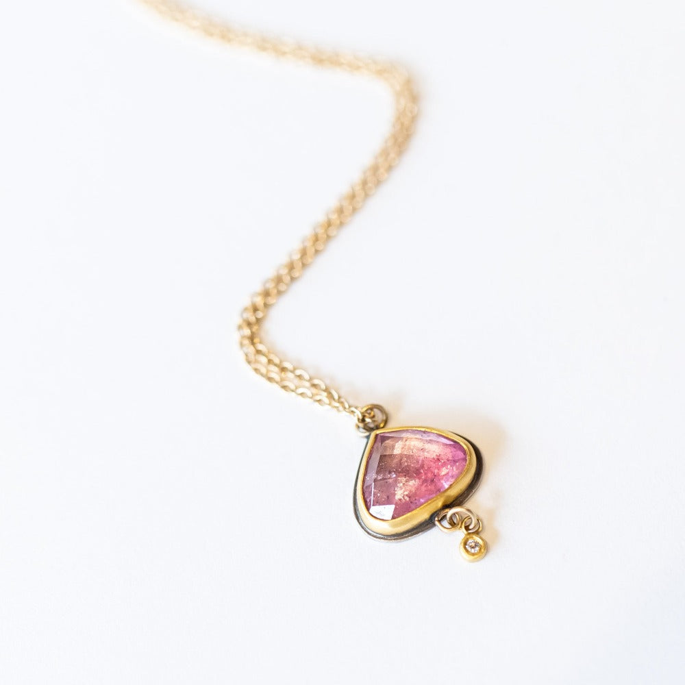 A yellow gold chain necklace with a wide teardrop, rose cut pink tourmaline in a 22k yellow gold bezel backed by oxidized sterling silver. A tiny bezel-set diamond charm dangles freely from the base.
