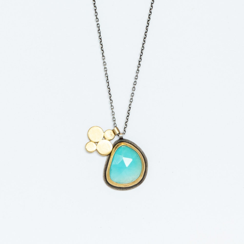 An asymmetrical, rose cut turquoise gemstone is bezel set in yellow gold and silver, accompanied by a flower-shaped gold charm in this sterling silver pendant necklace.