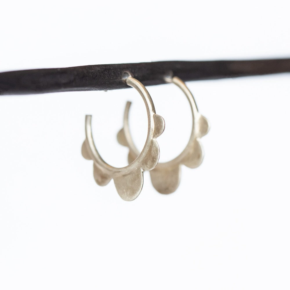 A pair of petite, brushed silver hoop earrings with flat scalloped design.