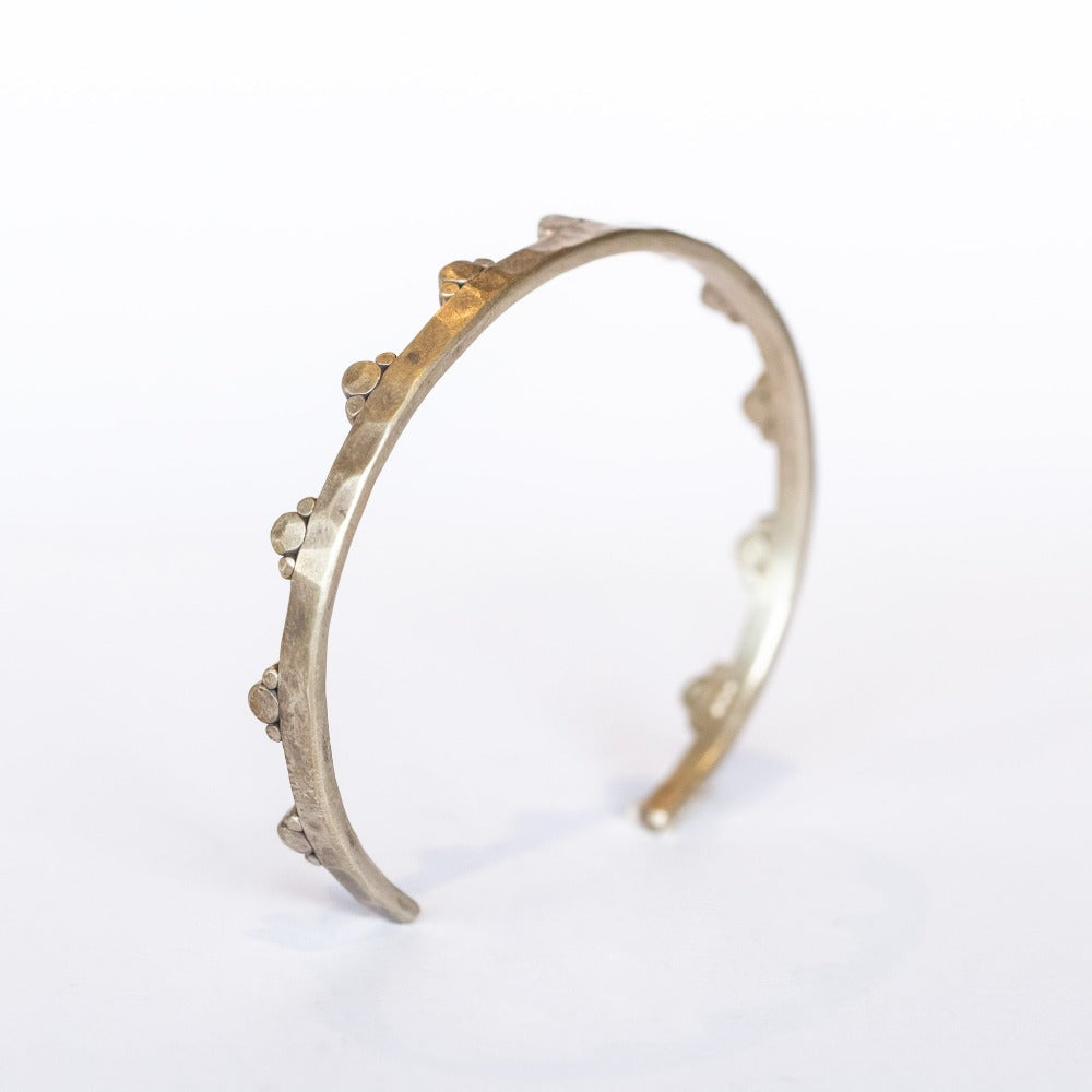 A hammered sterling silver cuff bangle bracelet with spaced out trios of silver dots along one edge.