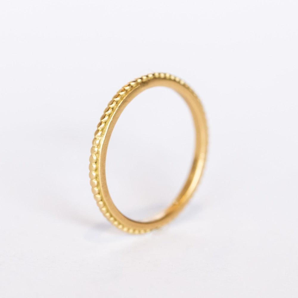 A yellow gold band with a tiny raised dot pattern from Ananda Khalsa. Side view.