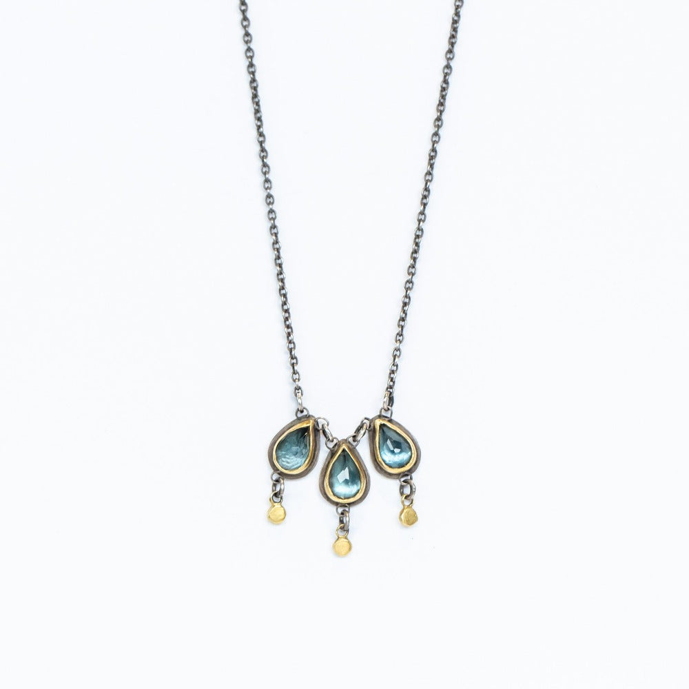 Three teardrop blue topaz gems are set in yellow gold, with tiny gold dot dangle accents, all on sterling silver backs with an oxidized silver chain.