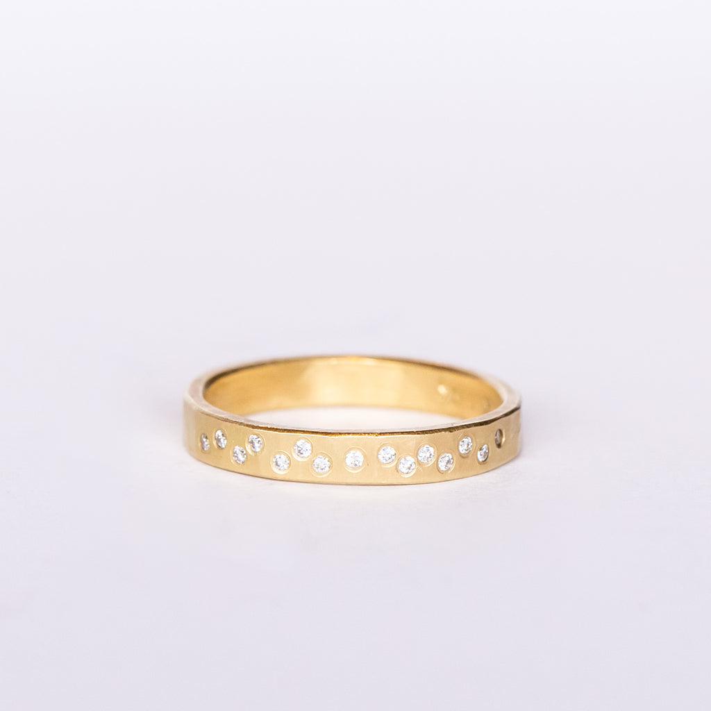 A hammered yellow gold wedding band set with a sprinkling of white diamonds from Ananda Khalsa. Front view.
