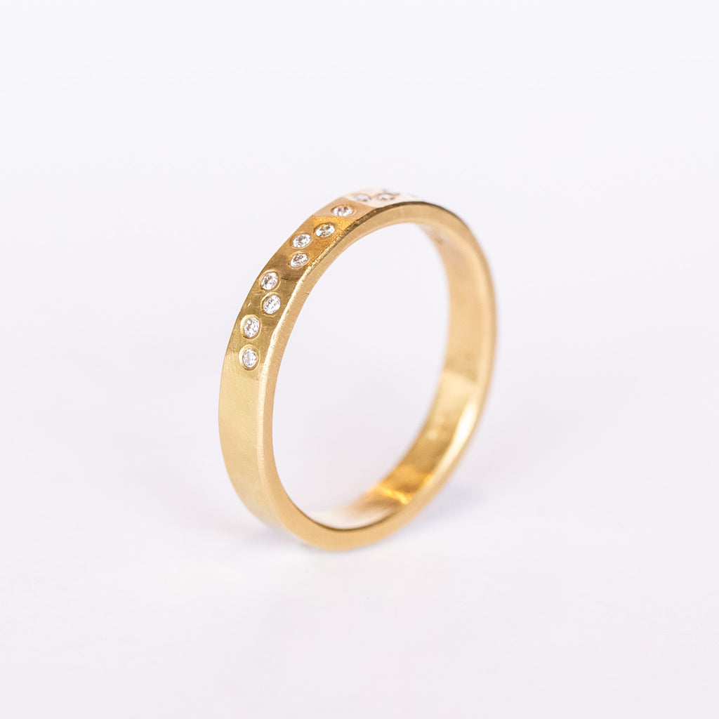 A hammered yellow gold wedding band set with a sprinkling of white diamonds from Ananda Khalsa. Side view.