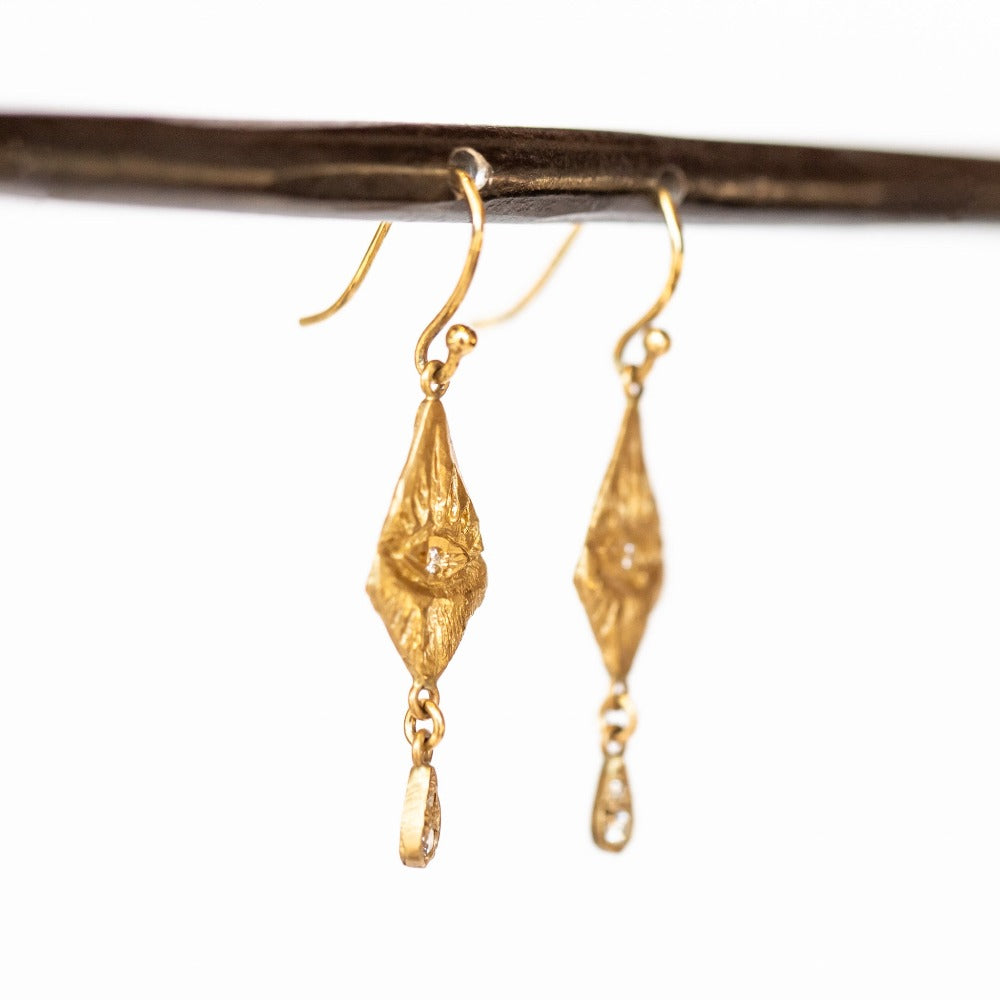 Gold diamond-shaped drop earrings with hand carved eye designs and diamond drops.
