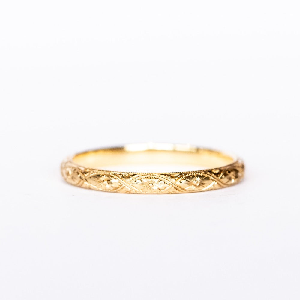 A half-round profile yellow gold wedding band with floral engraving all the way around.