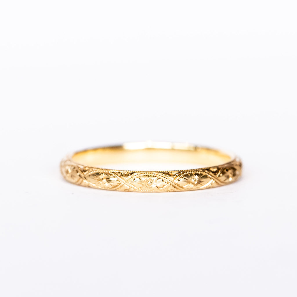 A half-round profile yellow gold wedding band with floral engraving all the way around.