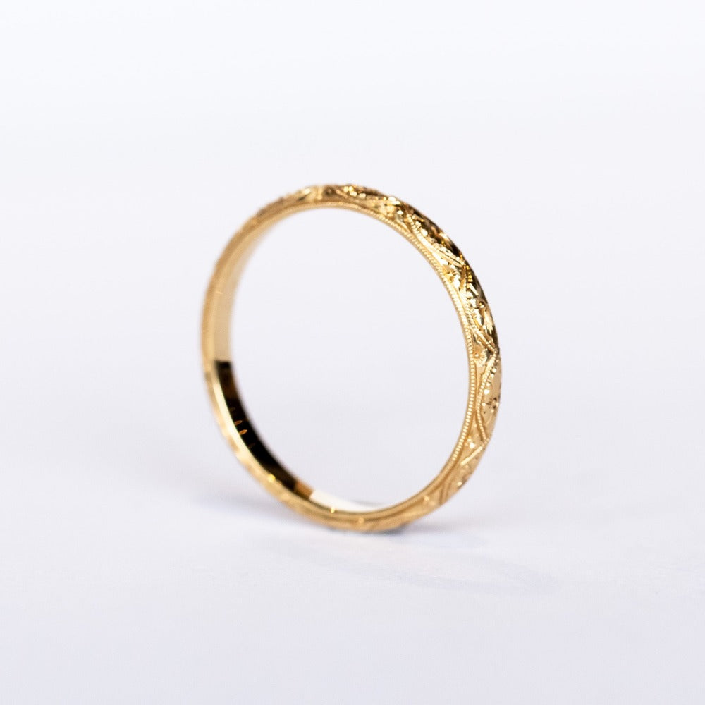 A half-round profile yellow gold wedding band with floral engraving all the way around.