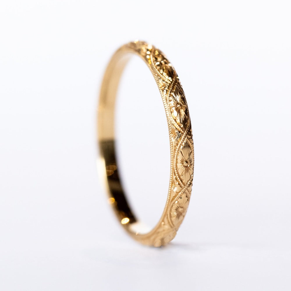 A half-round profile yellow gold wedding band with floral engraving all the way around.