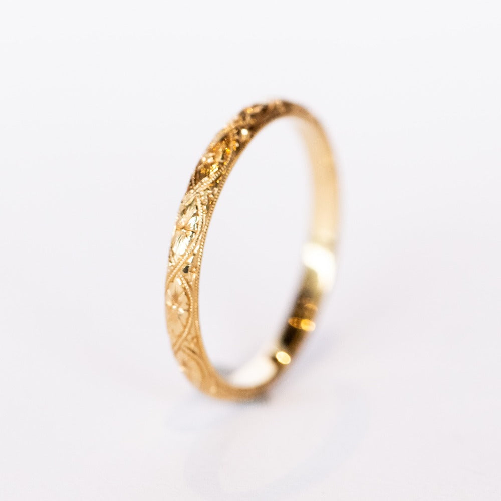 A half-round profile yellow gold wedding band with floral engraving all the way around.