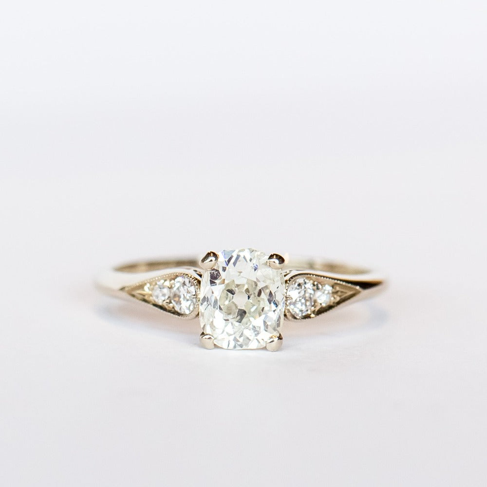 A diamond engagement ring with an old mine cushion cut center stone, raised cathedral shoulders with accent diamonds, in 18k white gold.