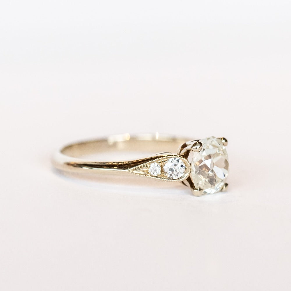 A diamond engagement ring with an old mine cushion cut center stone, raised cathedral shoulders with accent diamonds, in 18k white gold.