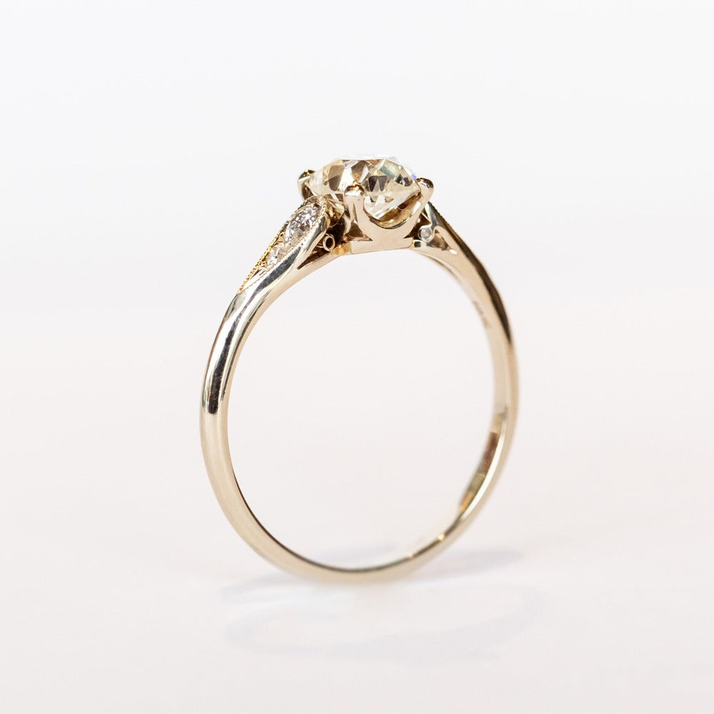 A diamond engagement ring with an old mine cushion cut center stone, raised cathedral shoulders with accent diamonds, in 18k white gold.