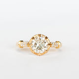 A diamond engagement ring with a round white center stone and 8 prong setting with vintage detailing. Each cathedral shoulder of the gold ring has three tiny accent diamonds.
