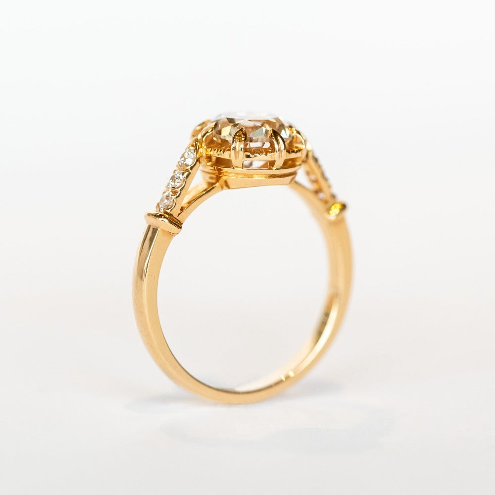 A diamond engagement ring with a round white center stone and 8 prong setting with vintage detailing. Each cathedral shoulder of the gold ring has three tiny accent diamonds.